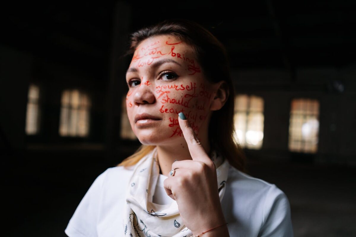 A woman with words written on her face poses in an artistic expression of activism and self-identity.